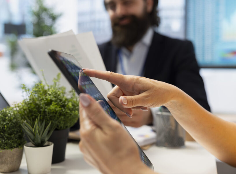 Financial advisor guiding clients in trading shares using software on tablet, making informed investment decisions. Agent offering advice on buying and selling stocks on device online, close up